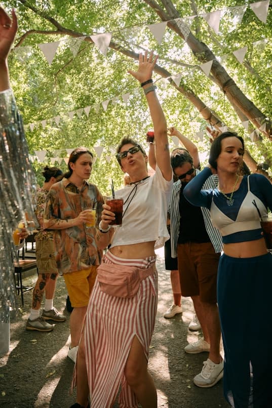 People dancing and drinking under string lights at an outdoor day event
